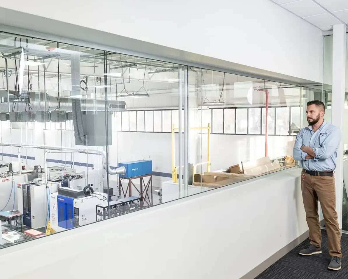 A man in work attire performs quality control as he stands and watches the inner workings of a machine shop.
